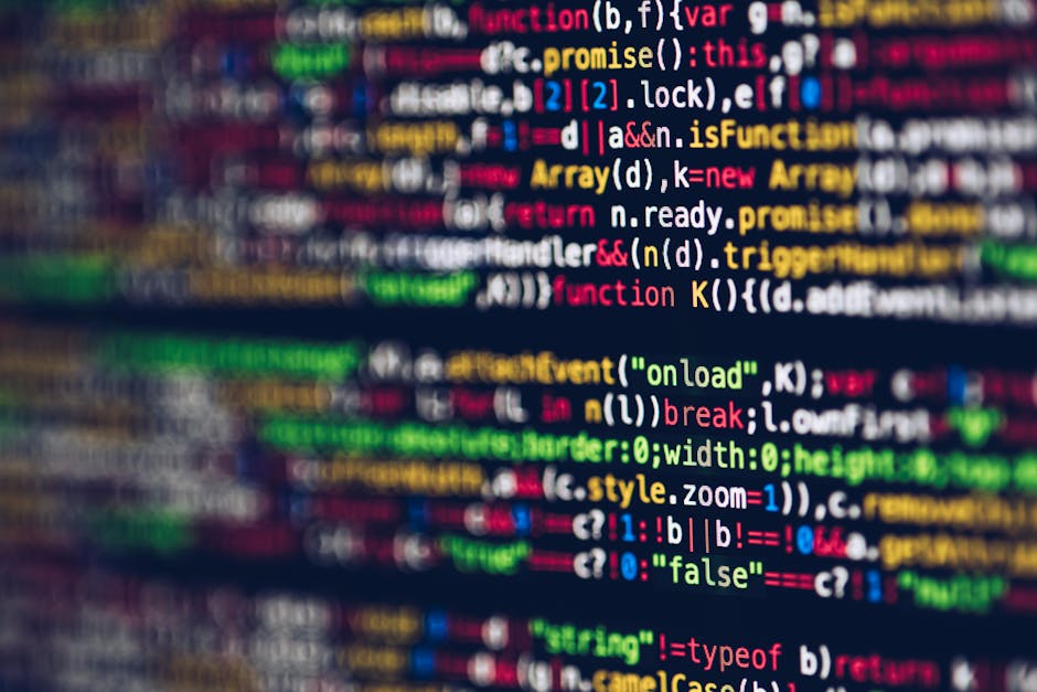 The image depicts a person working at a desk with a laptop displaying lines of colorful programming code. The individual, seen from behind, is using a stylus or pen to interact with the device, which 